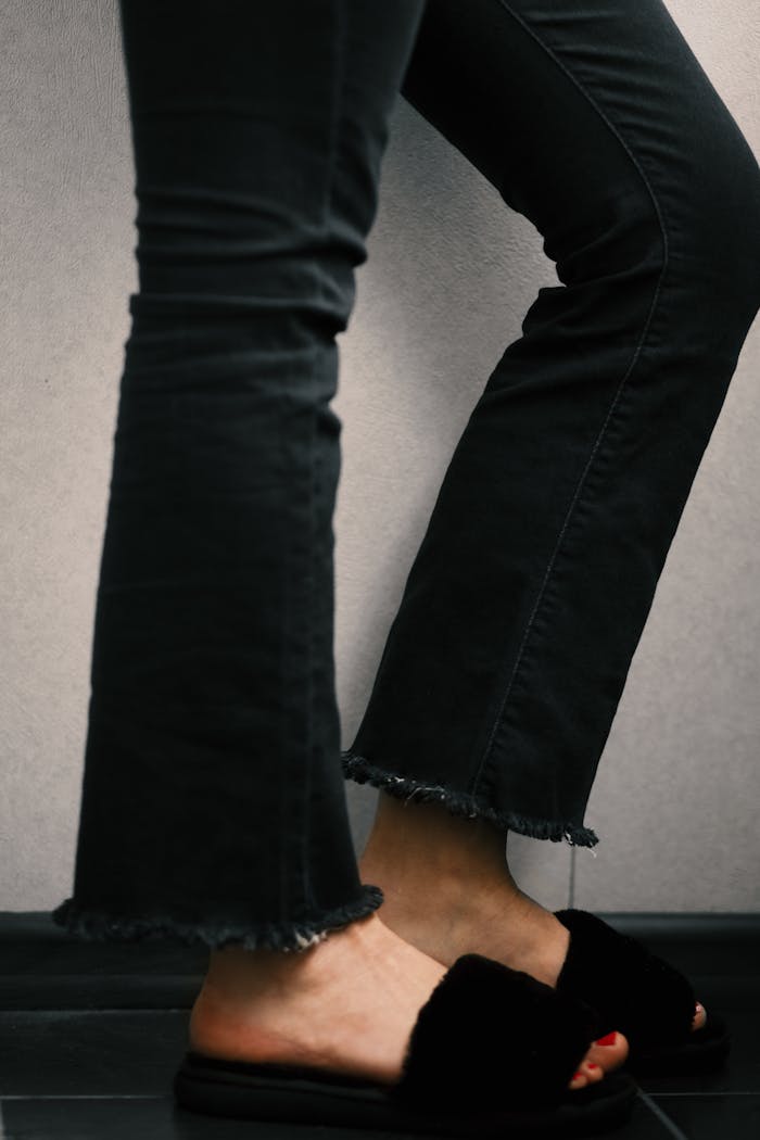 Stylish casual fashion capture featuring frayed denim jeans and black fur slippers.
